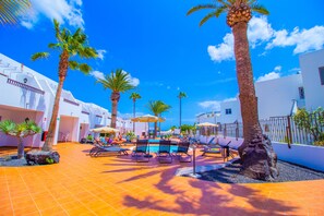 A poolside area with lounge chairs, palm trees, and a clear blue sky.