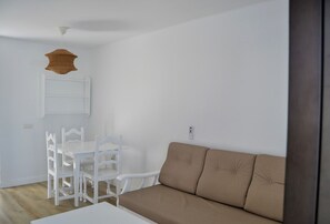 A minimalist living space with a white table, two white chairs, a beige sofa, and a white ceiling light fixture. - Apartamentos Flamingo (Tías)