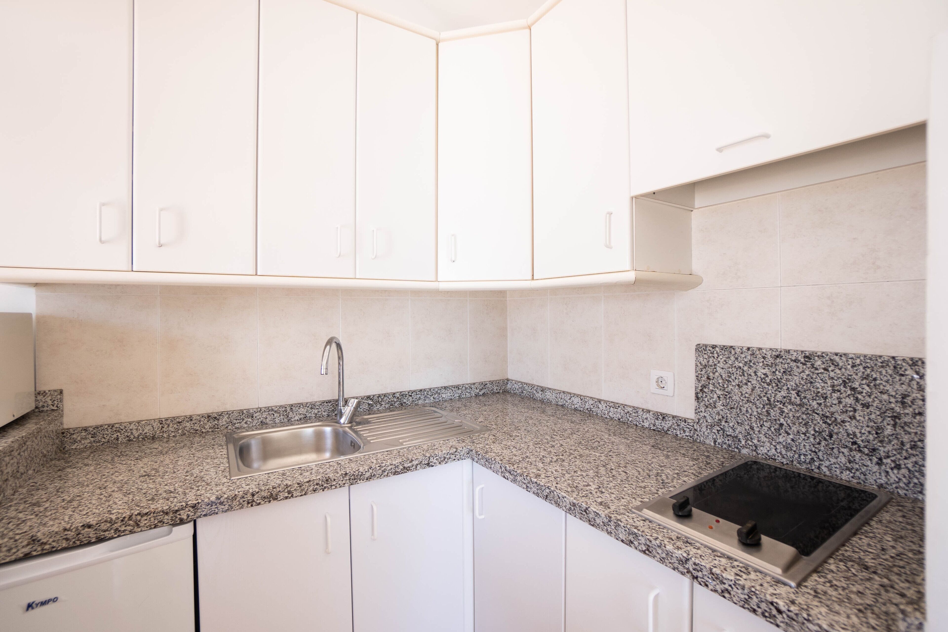 A kitchen with white cabinets, a granite countertop, a stainless steel sink, and a black stovetop.