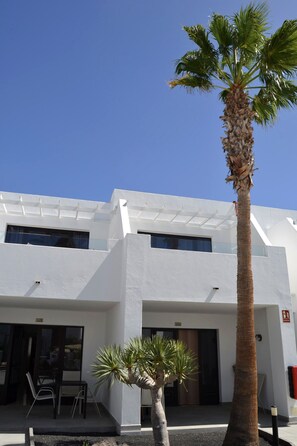 Un edificio moderno con fachada blanca, varias ventanas y una palmera en primer plano.
