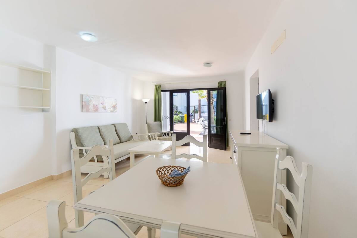 Un salón moderno con un sofá blanco, una mesa de comedor con una cesta y un televisor montado en la pared.