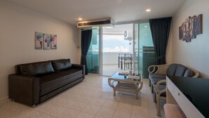 Una sala moderna con un sofá, una mesa de centro y un mueble para televisor. Se ve un balcón con vistas a un paisaje urbano.