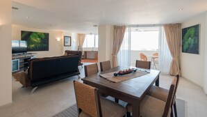 Una sala de estar moderna con comedor, sofá, televisor y ventanas grandes con cortinas.