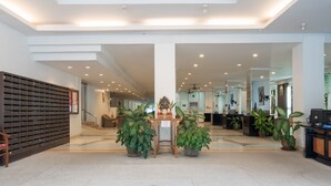 Un vestíbulo amplio con mostrador de recepción, plantas en macetas y un panel de buzones.