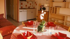 Eine kleine Küche mit Mikrowelle, Spüle und Schränken. Ein Esstisch ist mit roten Schüsseln und einer Blumenvase gedeckt.