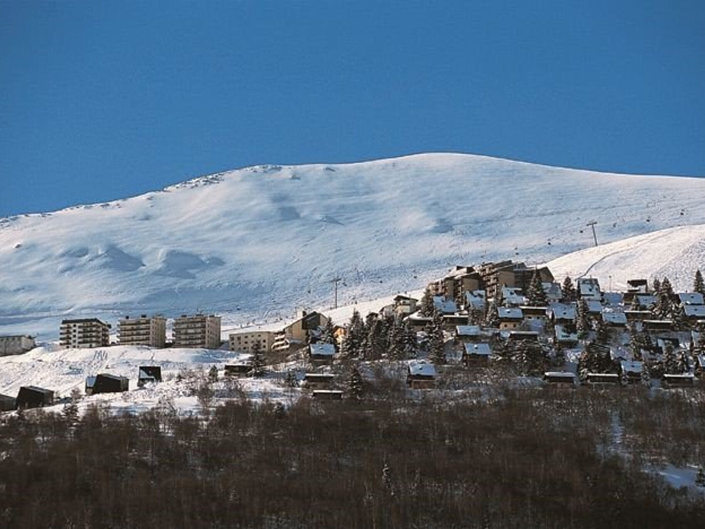 A snow-covered mountain with a town at its base, featuring buildings and a ski lift.