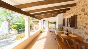 A covered patio with wooden benches and tables, stone walls, and a view of the garden. - CAN MORANTA ( VERD ). Beautiful villa near Pollensa (Alcúdia)