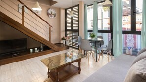 Una sala de estar con escalera de madera, televisor, mesa de centro y comedor con sillas y una mesa.