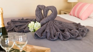 Una cama con una toalla doblada en forma de cisne, un ramo de flores y dos copas de vino sobre una bandeja.