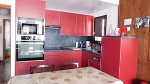 Cocina compacta con armarios rojos, microondas, horno y mesa de comedor con mantel estampado.