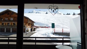 Vista desde un balcón con un edificio de madera con el rótulo 'BAR RESTAURANT te Chamois' y una montaña nevada al fondo.