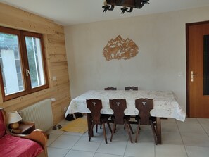 Ein Essbereich mit Tisch, Stühlen, einem Heizkörper, einem Fenster und einer Tür.