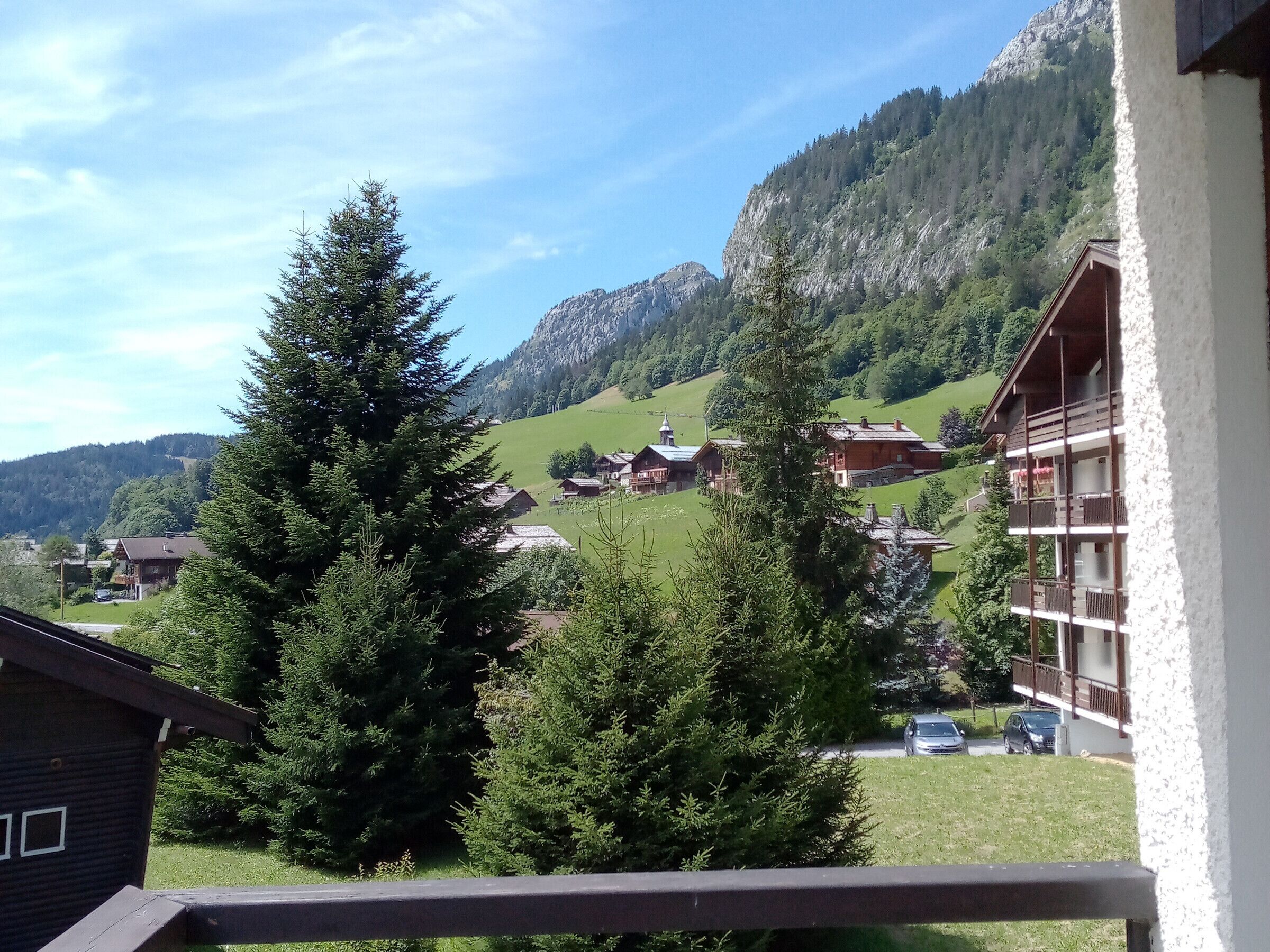 A mountain village with traditional wooden houses, a church, and a modern building with balconies.