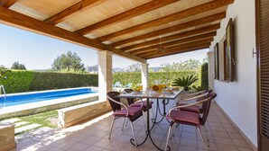 Eine überdachte Terrasse mit Pool, Sitzgelegenheiten im Freien und Blick auf die Landschaft.