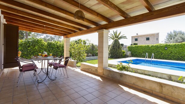 Eine überdachte Terrasse im Freien mit Pool, Sitzbereich und Blick auf die umliegende Natur und Gebäude.