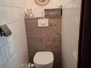 Ein kleines Badezimmer mit Fliesen, einer Toilette, einem Handtuchspender und einem dekorativen Wandbild.