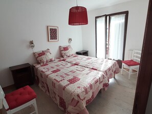 Ein Schlafzimmer mit zwei Betten, einer roten Hängelampe, einem gerahmten Bild an der Wand und einem Fenster mit Vorhängen.