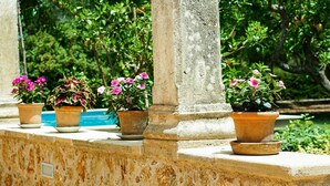 Une balustrade en pierre, agrémentée de plantes en pot, et une piscine en arrière-plan.