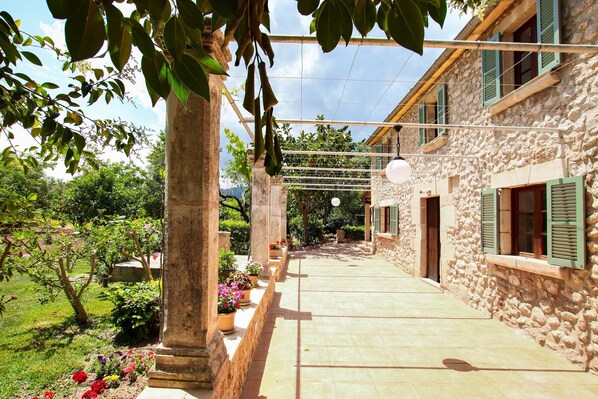 A stone building with a covered outdoor area, potted plants, and a clear sky.