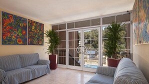 A sunlit living room with a striped sofa, two potted plants, and a sliding glass door leading to a balcony. - PINOS ALTOS 02. Lovely apartment in Cala San Vicenç (Cala San Vicente)