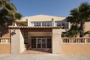 A two-story building with a beige facade, large windows, and a tiled entrance.