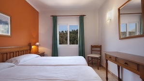 A bedroom with a bed, a chair, a desk, a window with curtains, a lamp, and a painting on the wall.