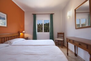 A bedroom with a bed, a chair, a desk, a window with curtains, a lamp, and a painting on the wall.