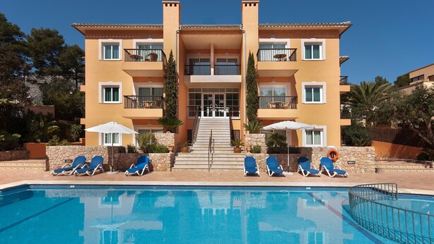 A multi-story hotel with a swimming pool, outdoor seating, and a staircase leading to the entrance. - PINOS ALTOS 02. Lovely apartment in Cala San Vicenç (Cala San Vicente)