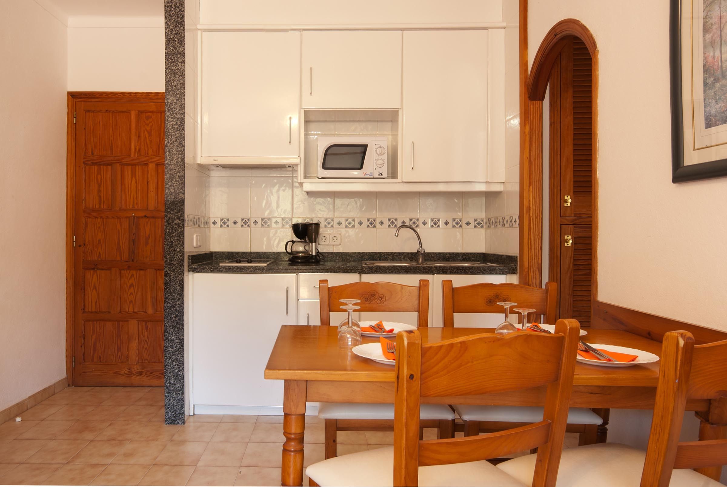 A compact kitchen with white cabinets, a microwave, and a dining table set for two.