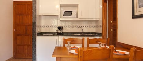 A compact kitchen with white cabinets, a microwave, and a dining table set for two.