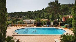 A swimming pool with lounge chairs and a covered area, surrounded by greenery and buildings.