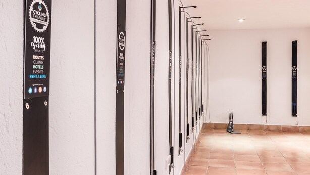 A wall-mounted bike rental station with a sign indicating 100% cycling services, including routes, climbs, hotels, events, and a bike rental option.