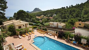 A pool area with sun loungers, a circular hot tub, and a view of a mountain and sea.