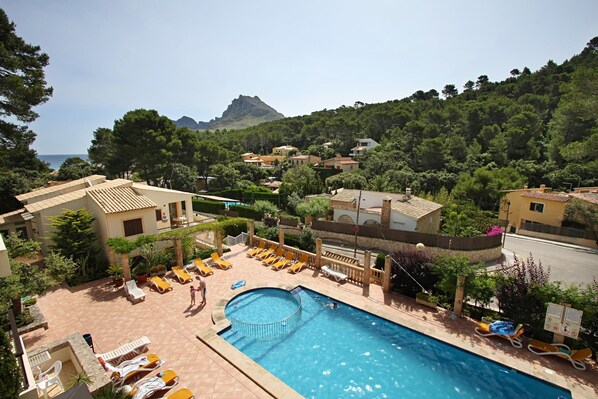 A pool area with sun loungers, a circular hot tub, and a view of a mountain and sea.