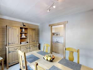 Un comedor con una mesa de madera, sillas y un frutero. Se ve una cocina a través de una puerta abierta.