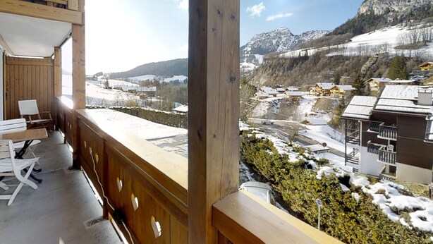 Ein hölzerner Balkon mit Blick auf eine verschneite Berglandschaft und ein Dorf darunter.