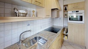 Une cuisine moderne dotée de plans de travail en granit, d’un évier en acier inoxydable, de meubles en bois et d’un four encastré.
