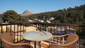 Ein Balkon mit Korbstühlen und einem Tisch, der auf eine Berglandschaft und ein Dorf blickt.