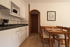 A kitchen with white cabinets, a microwave, and a coffee maker. There is a dining table with chairs and a framed picture on the wall. - PINOS ALTOS 11. Beautiful apartment in Cala San Vicenç (Cala San Vicente)