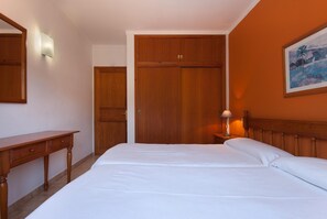 A bedroom with a wooden wardrobe, a bedside table with a lamp, and a bed with white linens.