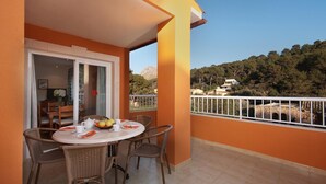 A balcony with a dining table and chairs, a view of a mountainous landscape, and a white railing.