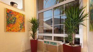 A hallway with a large window, a colorful abstract painting, and two potted plants.