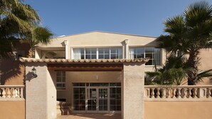 A two-story building with a beige facade, large windows, and a tiled entrance.