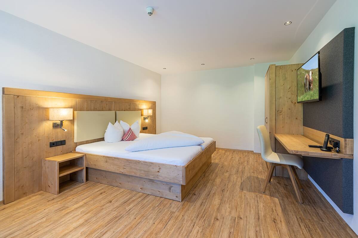 Un dormitorio moderno con una cama de madera, mesitas de noche, un escritorio y un televisor montado.
