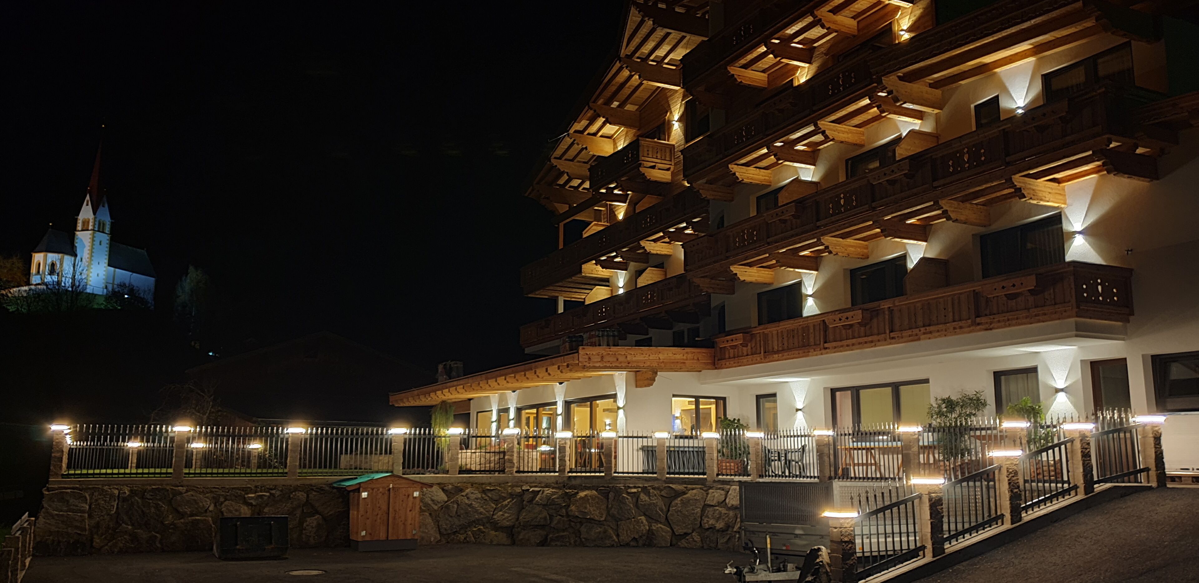 Ein mehrstöckiges Hotel mit Balkonen, einer Steinmauer und einer beleuchteten Fassade.