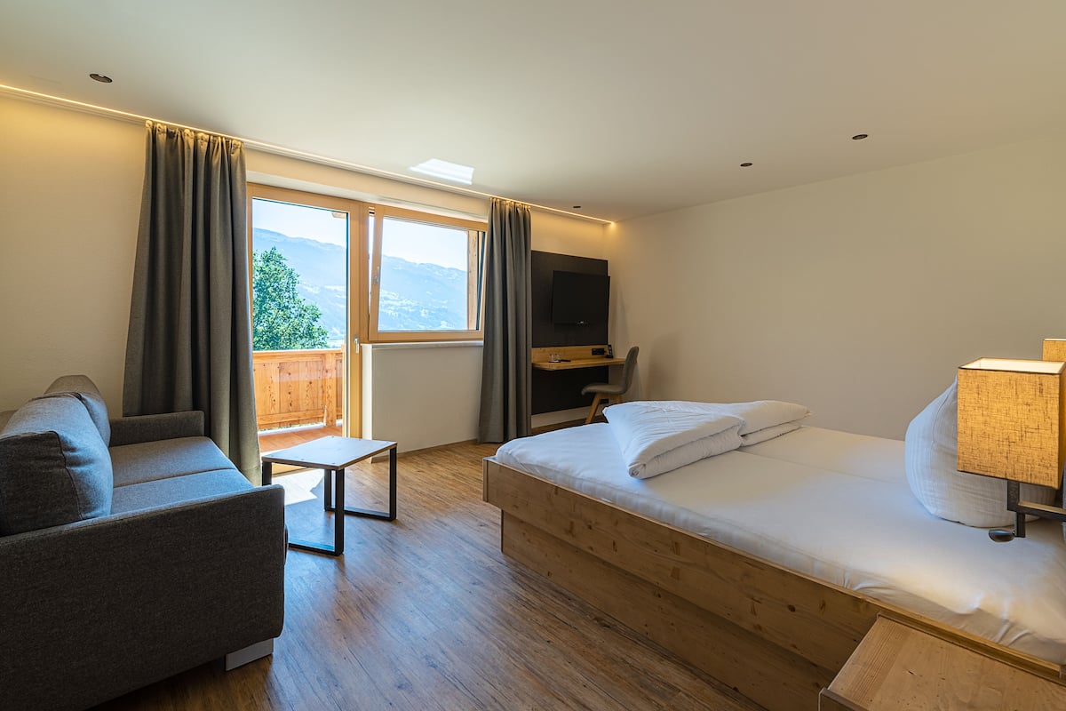 Una habitación de hotel moderna con una cama de madera, un sofá, un escritorio y un televisor.