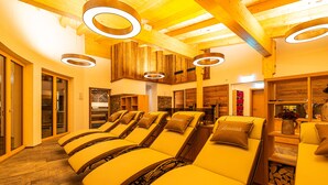 A spa area with multiple sun loungers, wooden ceiling beams, and circular light fixtures. - Hotel Garni Romantik (Fuegenberg)