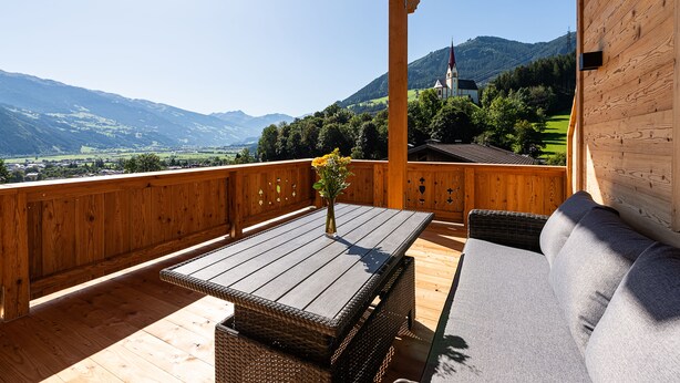 A wooden deck with a table and a sofa, overlooking a mountainous landscape. - Hotel Garni Romantik (Fuegenberg)