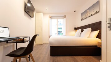 Hotelkamer met een bed, bureau met een laptop, stoel, tv aan de muur en raam met uitzicht op gebouwen.