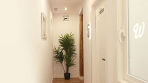 Un pasillo estrecho con una planta en maceta, una puerta de madera y una pared blanca con un letrero.